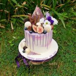 Purple chocolate drip cake with macarons, chocolates, fresh flowers and berries