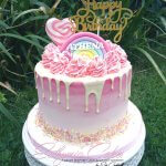 Pink ombre birthday drip cake with butter cream swirls, rainbow and lollipops